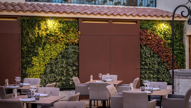 An outdoor dining area with tables and chairs, surrounded by vertical gardens with various plants.