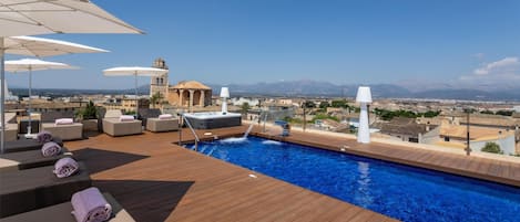 A rooftop pool with lounge chairs, umbrellas, and a hot tub.