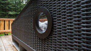 Une terrasse en osier agrémentée d’un miroir rond et d’un banc en bois.