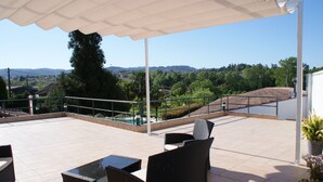 A covered outdoor seating area with wicker furniture and a view of a hillside. - Casa Fundevila (Vila Verde)