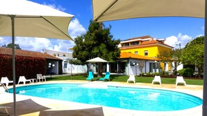 A swimming pool with lounge chairs and umbrellas, surrounded by a well-maintained lawn and a yellow building. - Casa Fundevila (Vila Verde)