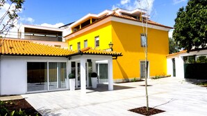 A modern yellow building with a tiled roof, a covered patio area, and a small garden. - Casa Fundevila (Vila Verde)