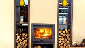A fireplace with a fire, flanked by shelves with logs and decorative items. - Casa Fundevila (Vila Verde)