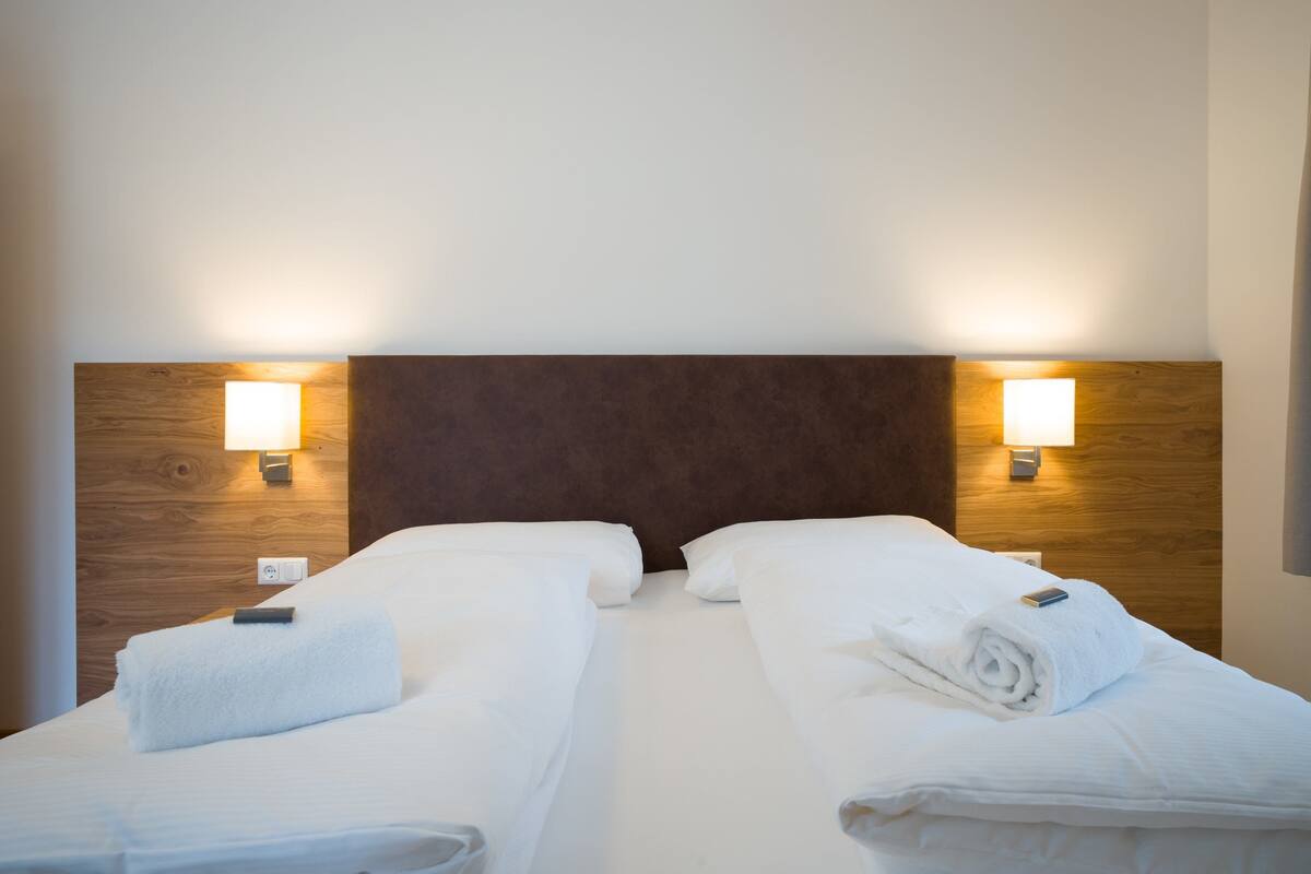 A hotel room with two single beds, wooden headboards, and bedside lamps.