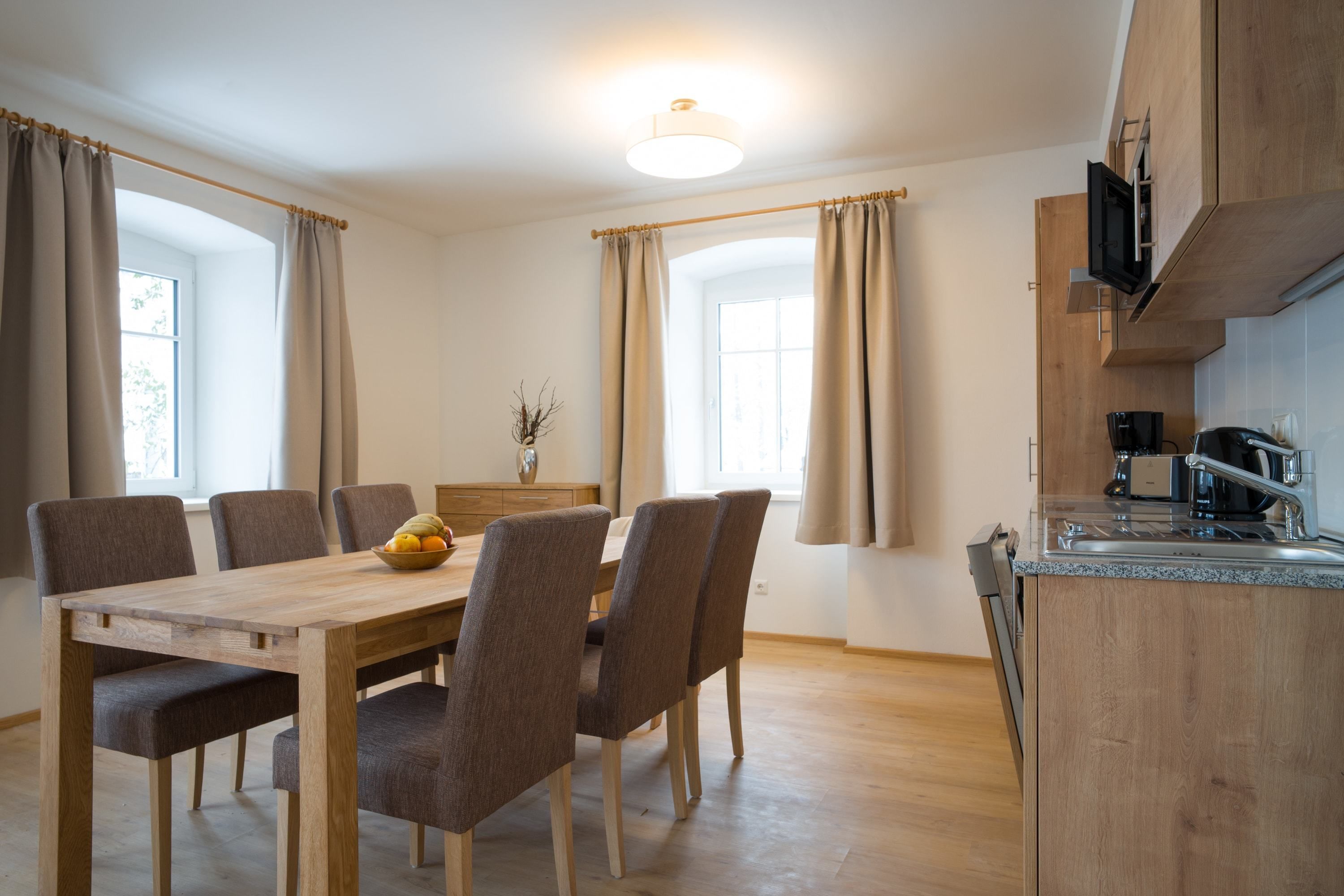 Una cocina moderna con armarios de madera, microondas integrado y un lavamanos de acero inoxidable.
