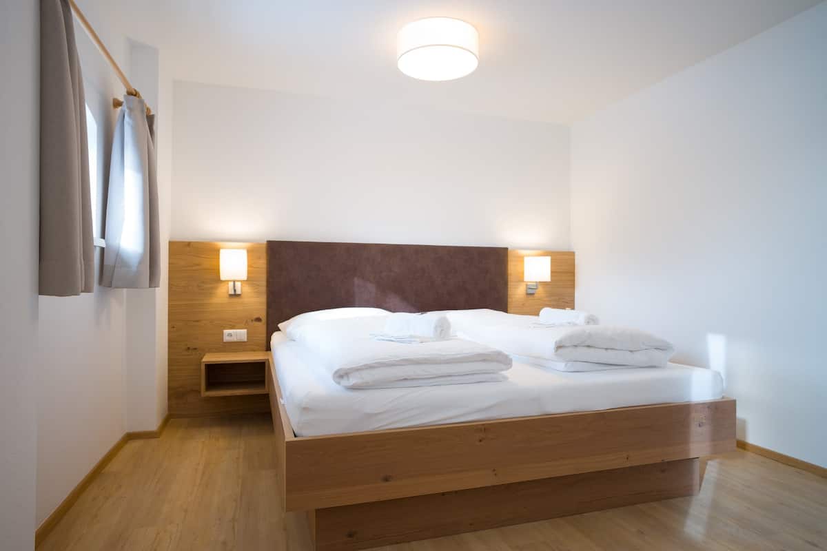 A neatly made bed with white linens and towels, a wooden headboard, bedside lamps, and a wooden nightstand.
