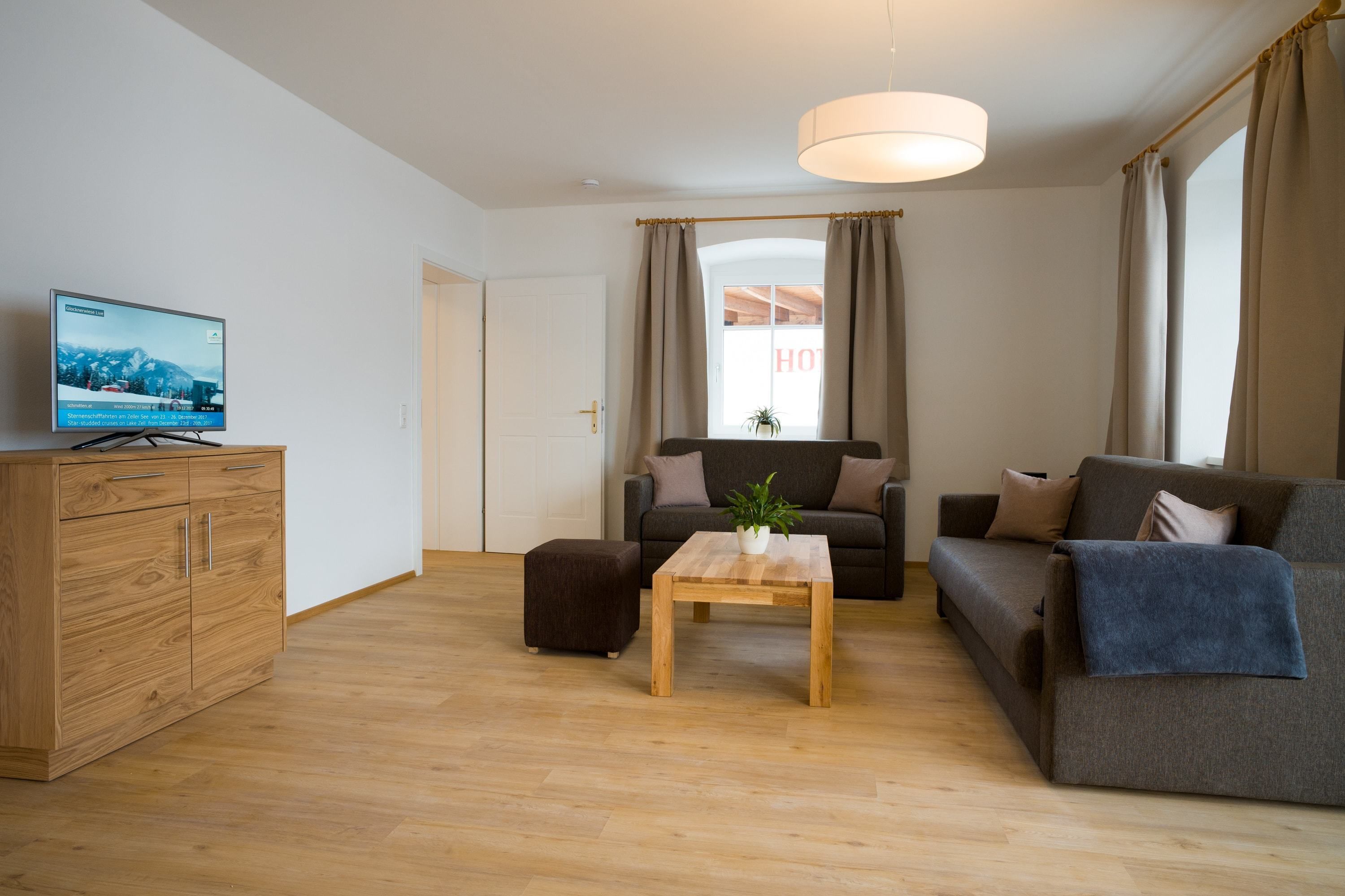 A modern living room with a wooden cabinet, a television, a sofa, a coffee table, and a window with curtains.