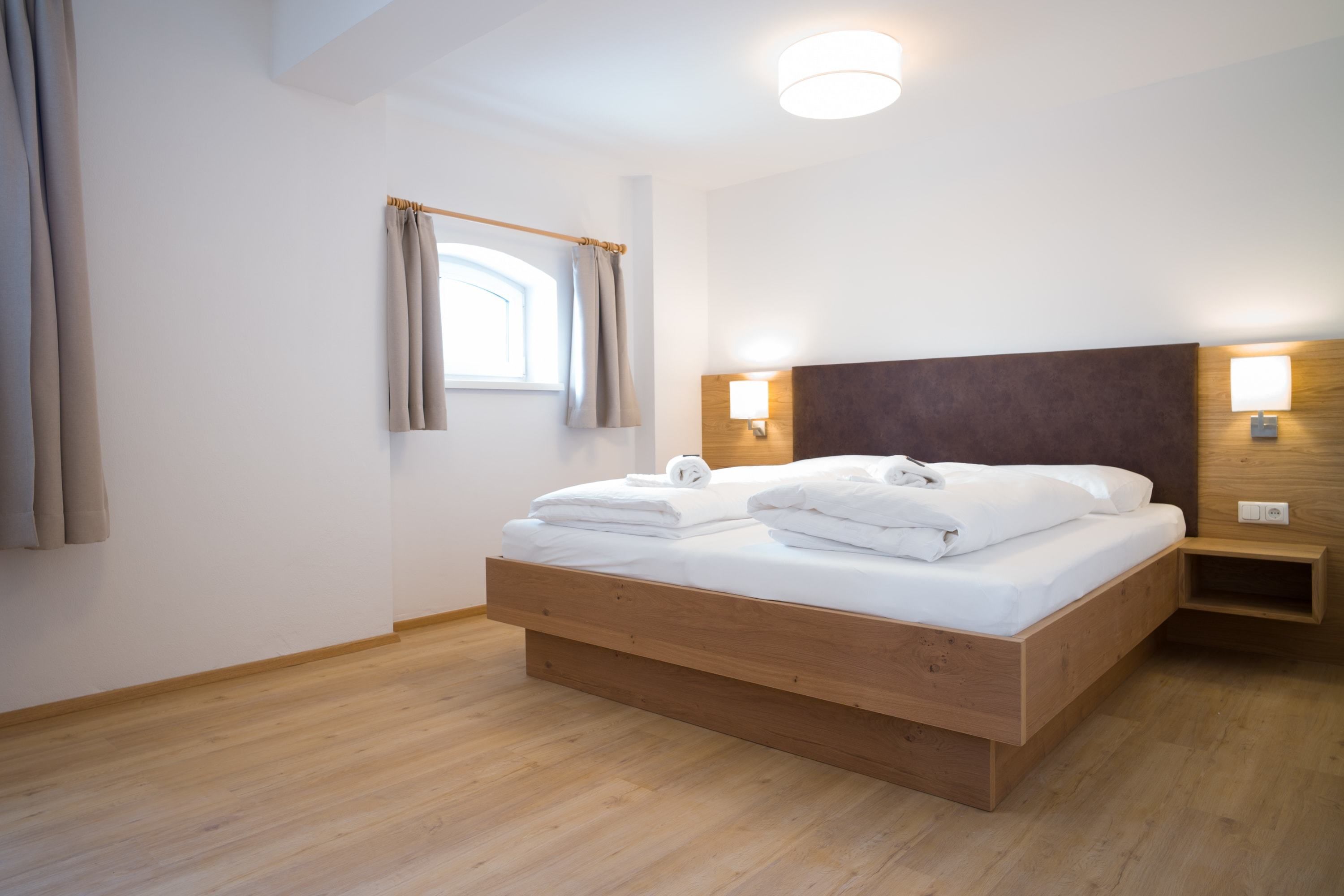 Une chambre à coucher moderne avec un lit en bois, des lampes de chevet et une fenêtre avec des rideaux.