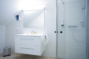 Un baño moderno con un tocador blanco, cabina de ducha de vidrio y espejo sobre el lavamanos.