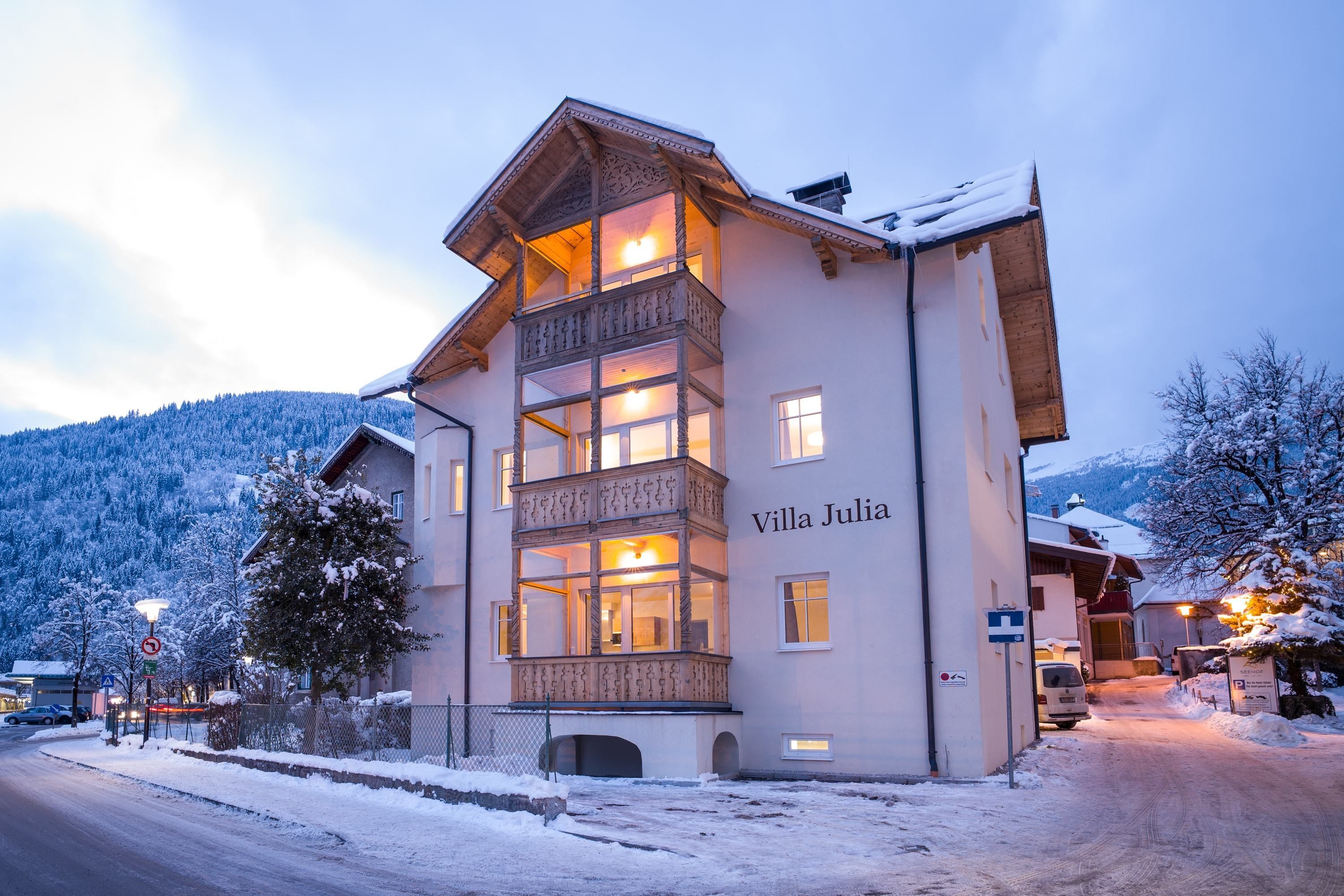 A multi-story building named Villa Julia with a balcony, snow-covered surroundings, and a mountainous backdrop.