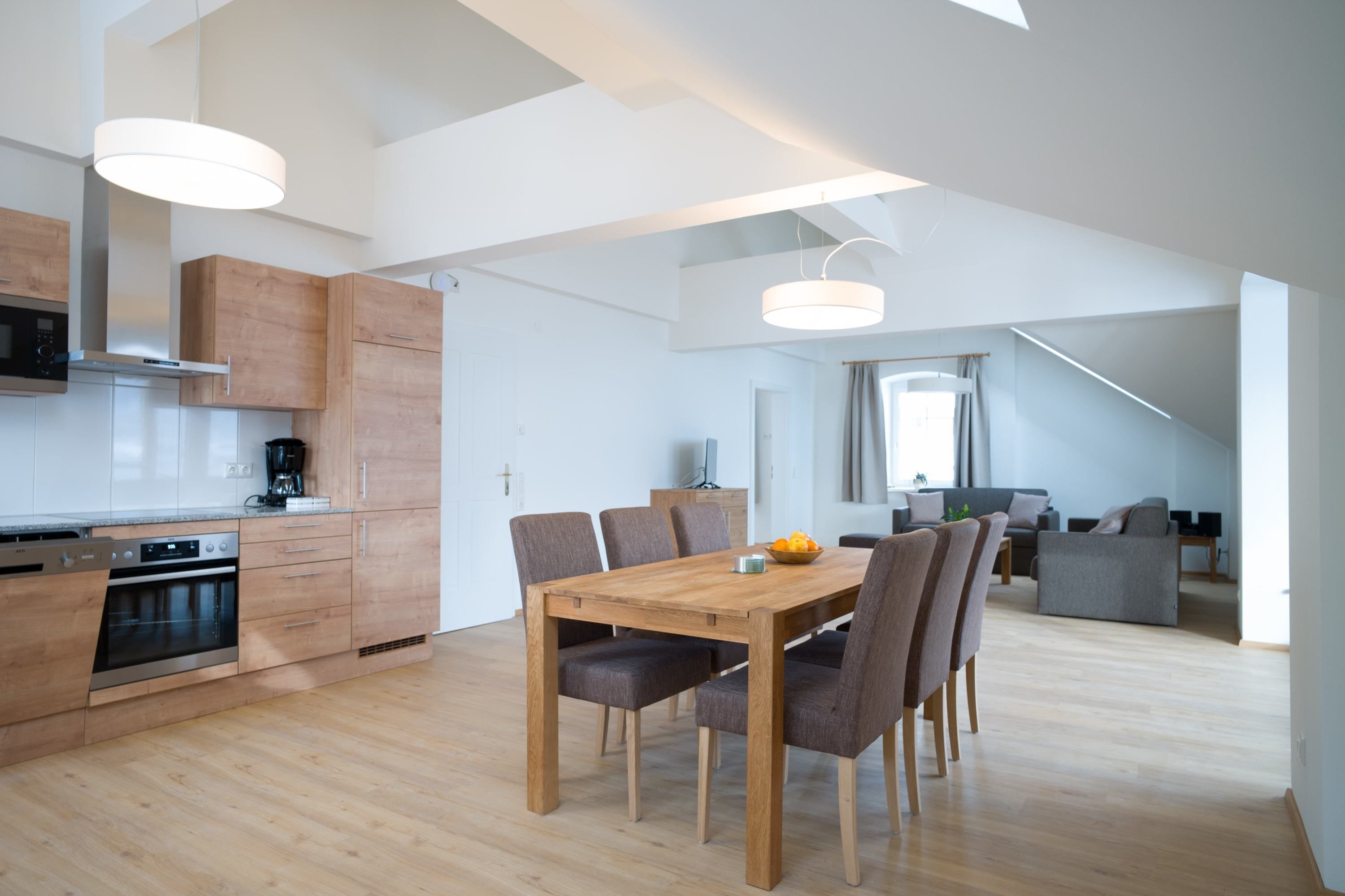 A modern kitchen with wooden cabinets, a dining table with chairs, and a staircase leading to a loft area.