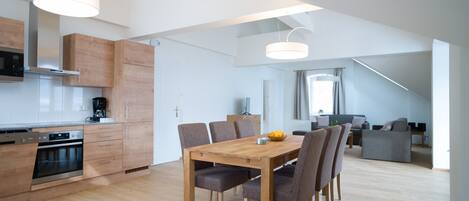 A modern kitchen with wooden cabinets, a dining table with chairs, and a staircase leading to a loft area.
