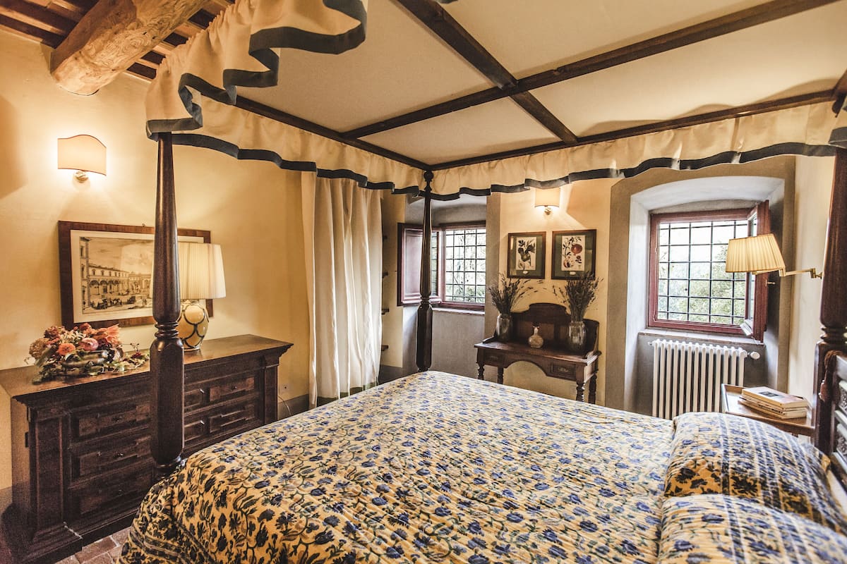 A traditional bedroom with a four-poster bed, a dresser, and a window with a view.
