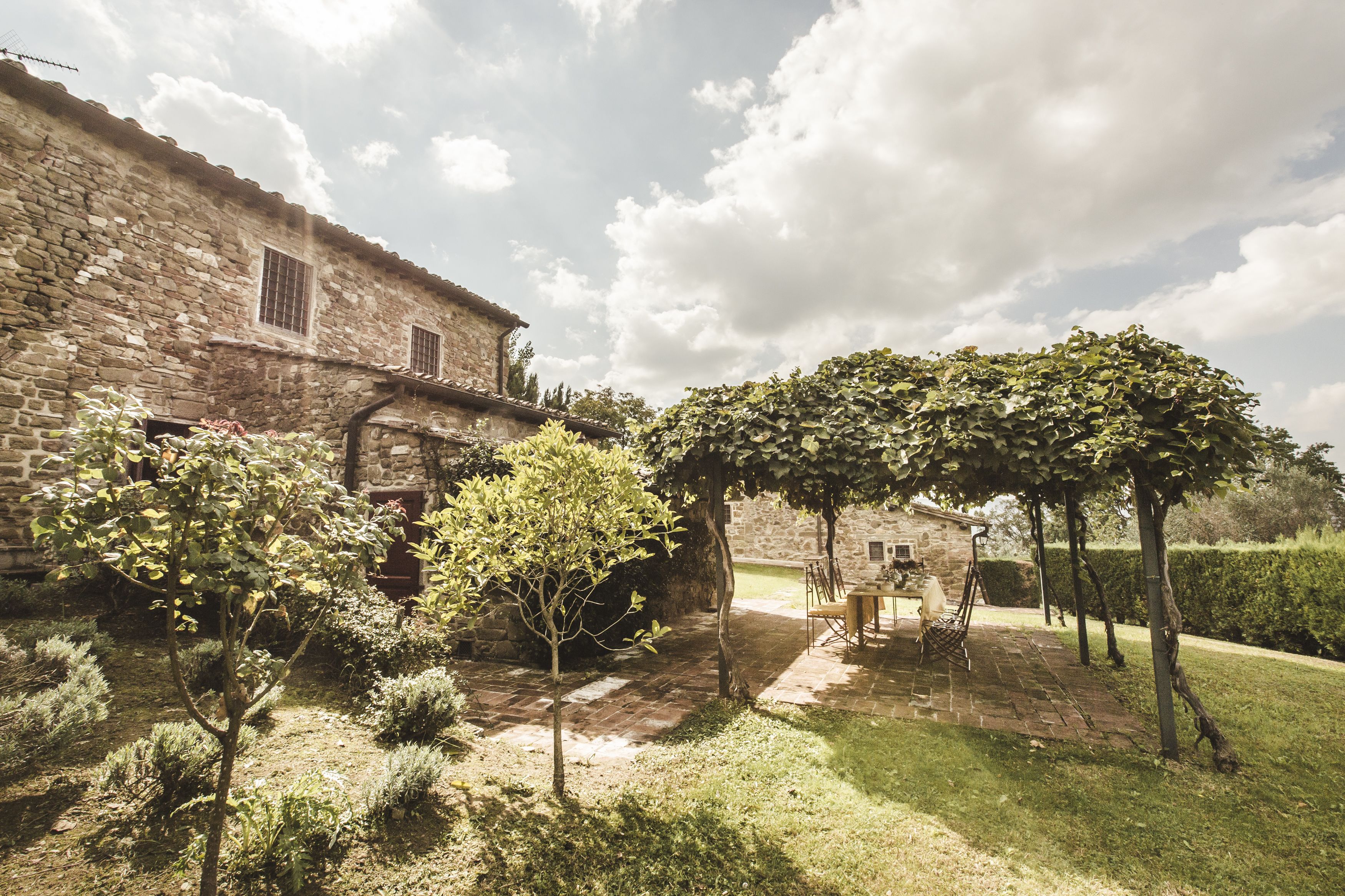 A stone building with a garden patio, a pergola, and a small table with chairs.