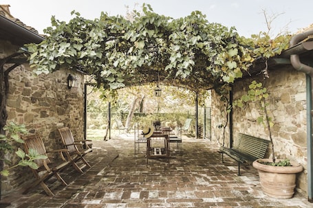 A covered outdoor seating area with stone walls, wooden furniture, and a pergola with vines.