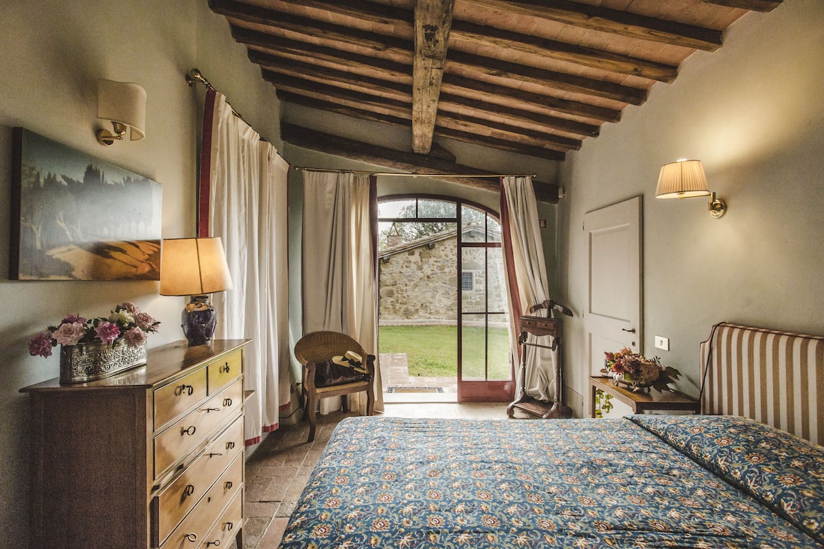 A bedroom with a bed, a dresser, a chair, a lamp, and a view of the outdoors.