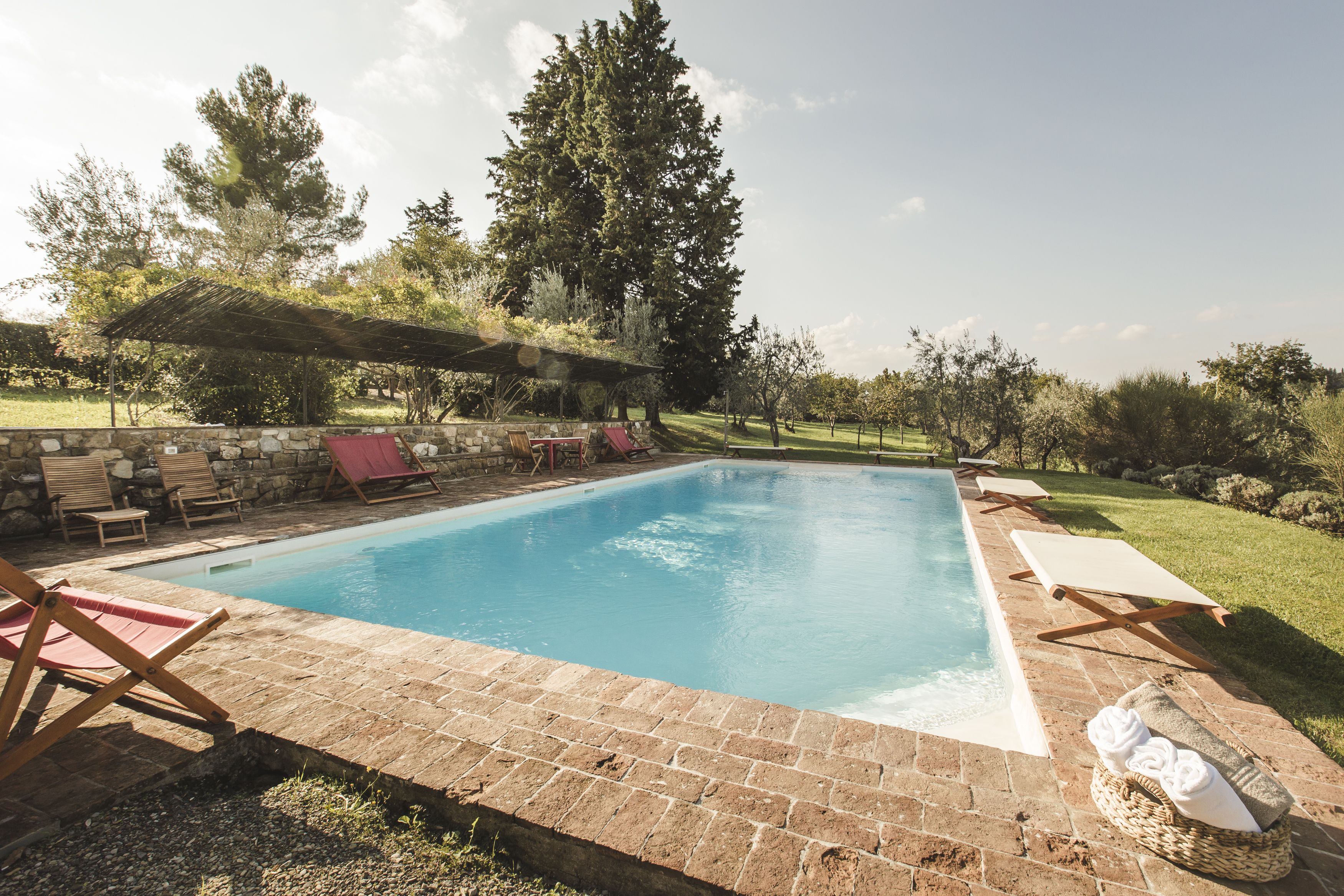 Une piscine rectangulaire bordée de briques, entourée de chaises longues et d’un mur en pierre.