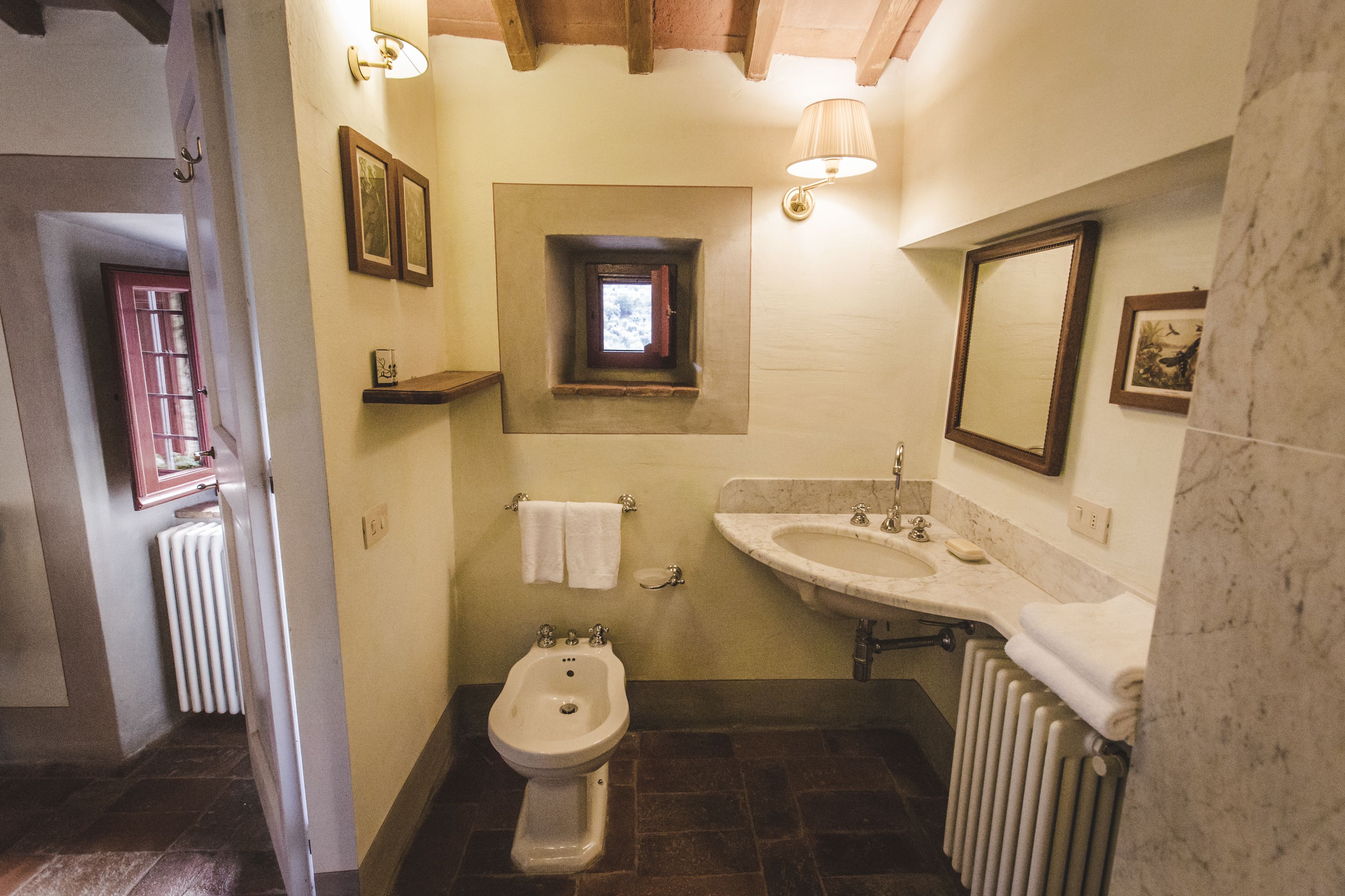 A bathroom with a bidet, a sink, a mirror, and a small window.