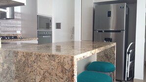 A kitchen with a granite countertop, stainless steel appliances, and teal stools. - H2 LUXURY 3 Bedroom Apartment (Cartagena)