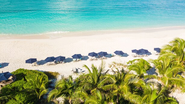 Een strand met wit zand, helder turquoise water en verschillende parasols.