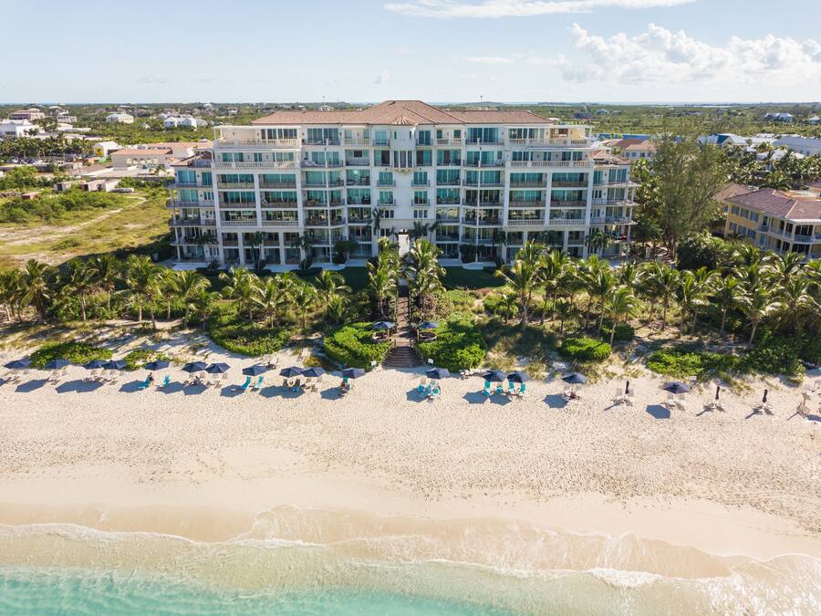 A multi-story hotel with a beach view, featuring a large pool area and numerous beach umbrellas.