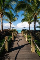 A wooden boardwalk leading to a beach with palm trees and a clear blue sky.