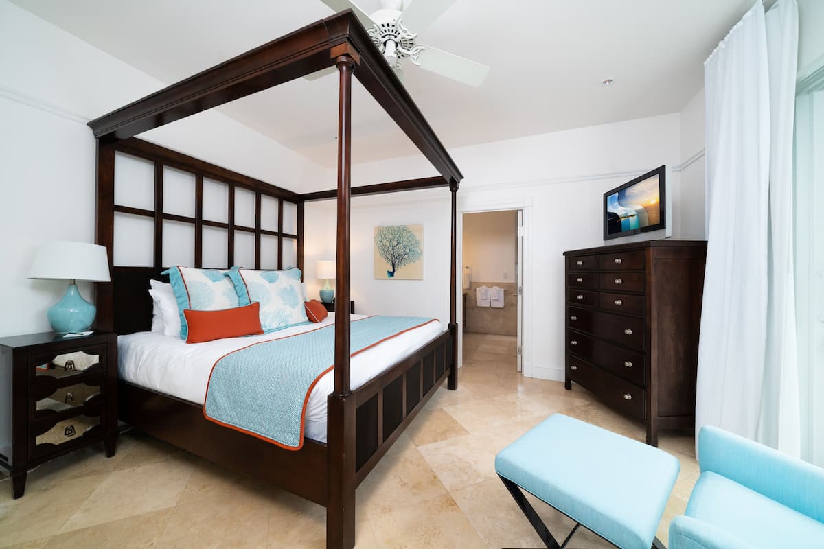A four-poster bed with a wooden frame, a bedside table with a lamp, a dresser, and a bench.