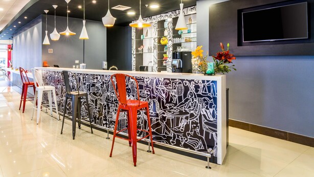 Un espace bar moderne avec un comptoir à motifs, des chaises rouges et blanches et des luminaires suspendus.