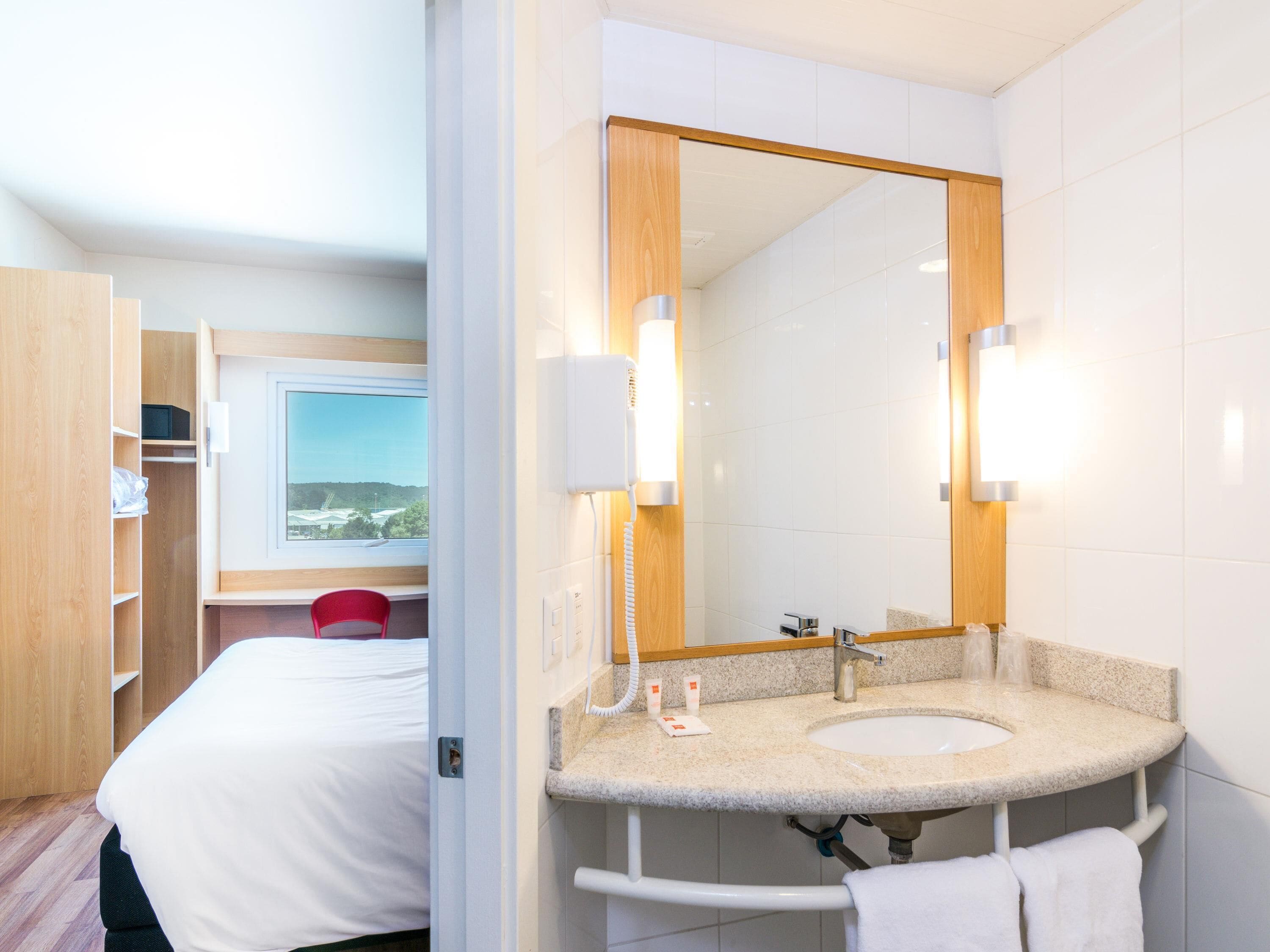 A hotel bathroom with a large mirror, a sink, and a toilet.