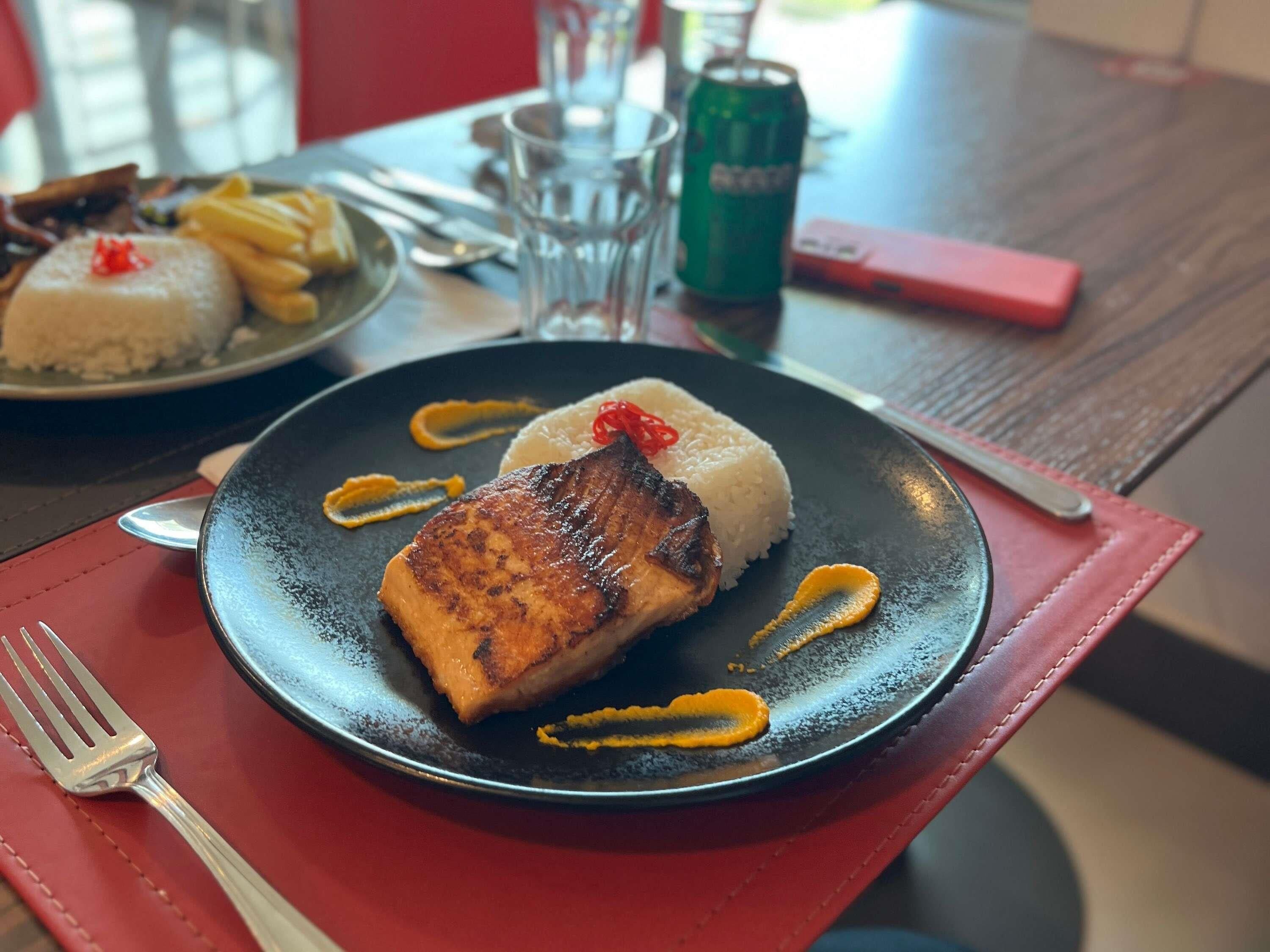 En tallerken med grillet fisk, ris og sauce på et bord.