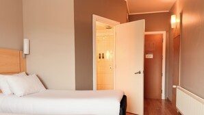 Une chambre d’hôtel avec deux lits, une tête de lit en bois, un mur blanc et une porte donnant sur une salle de bain.