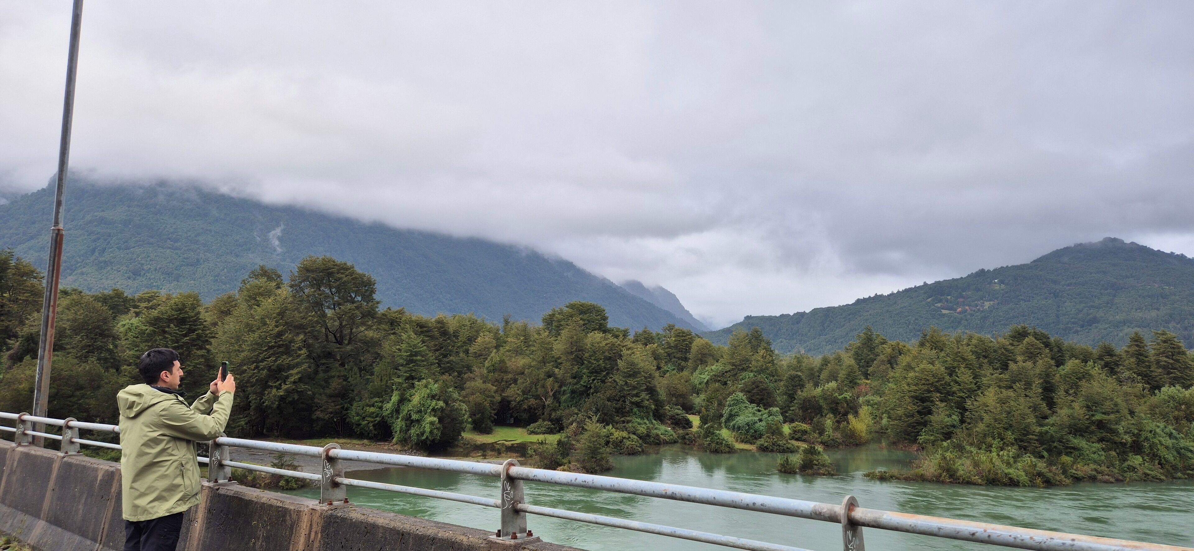Une personne prend une photo d’une rivière, avec des montagnes en arrière-plan.