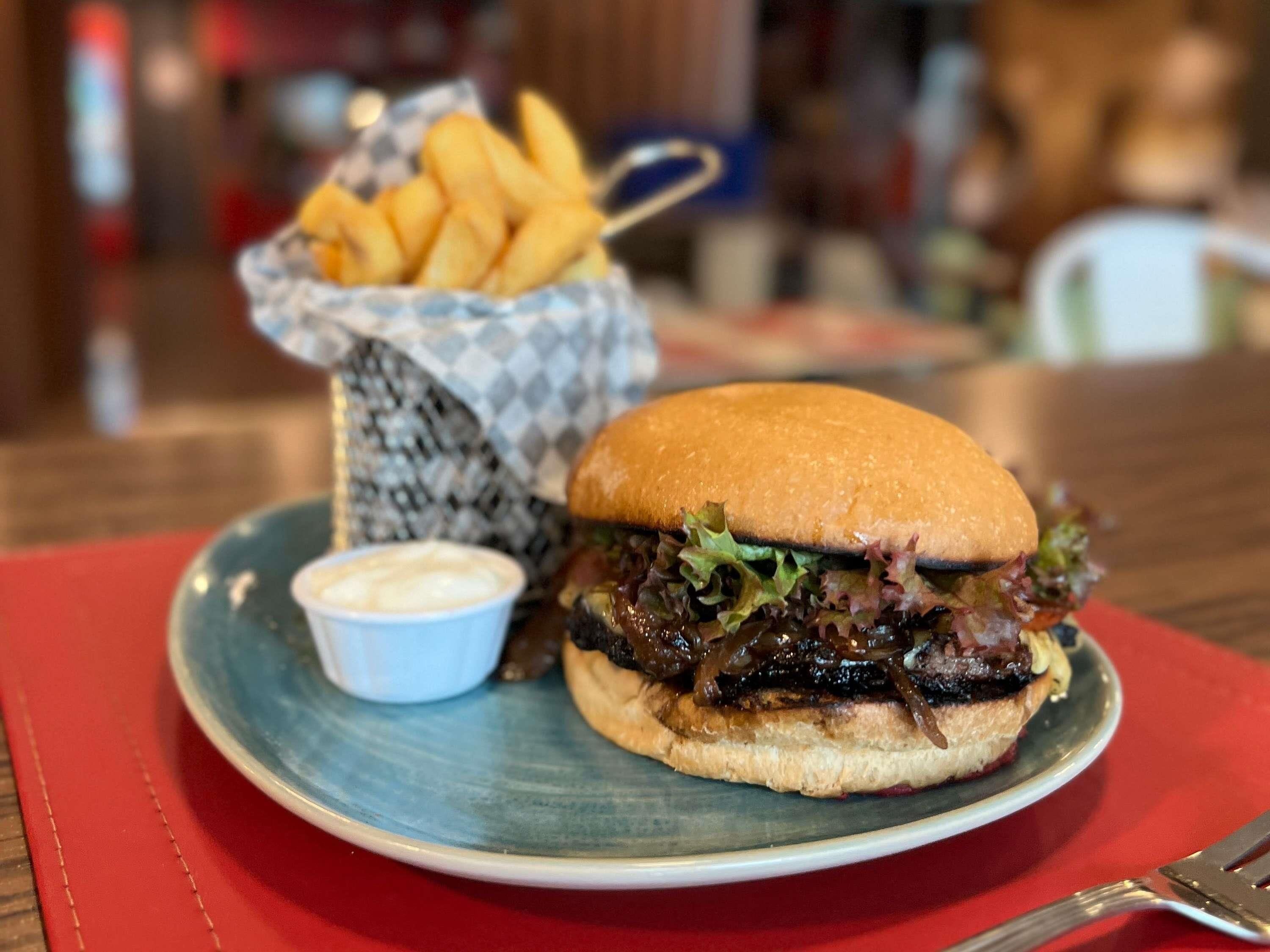 A plate with a burger and fries, a small cup of sauce, and a basket of fries.