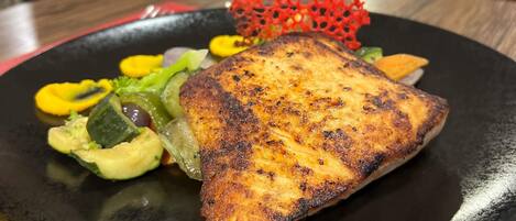 Un plato con pescado a la parrilla, verduras y un detalle decorativo rojo.