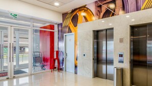 Un hall d’entrée moderne avec une porte d’entrée en verre, un fauteuil rouge, un ascenseur et une fresque murale.