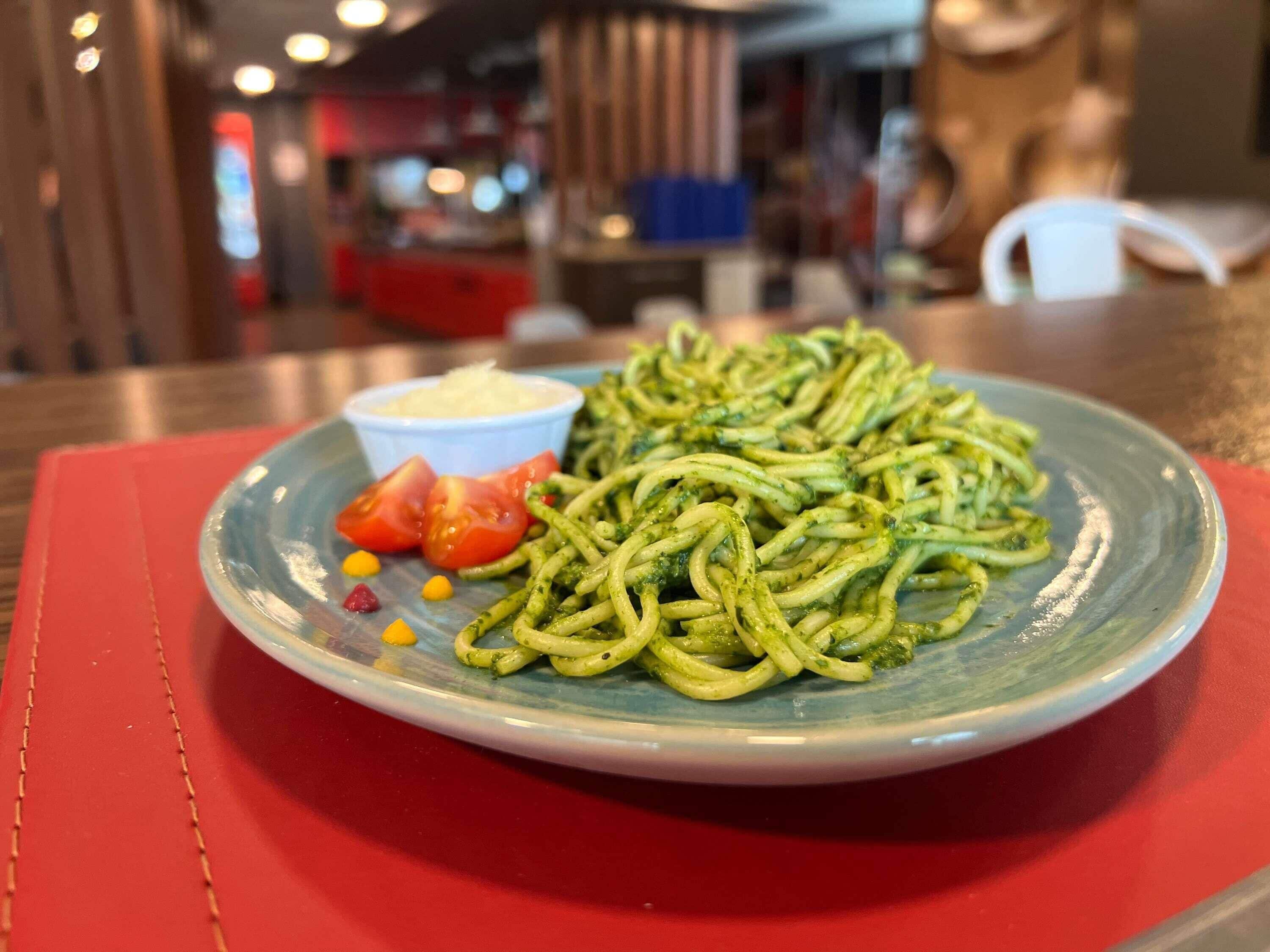 Une assiette de pâtes, accompagnée d’une sauce et de légumes, est posée sur une table.
