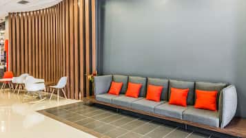 Un área de recepción moderna con un sofá gris, cojines naranjas y sillas blancas.