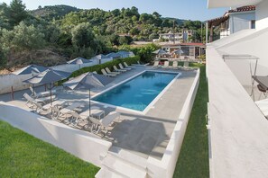 A swimming pool with sun loungers and umbrellas, surrounded by a white wall and a grassy area. - Dream House (Skiathos)