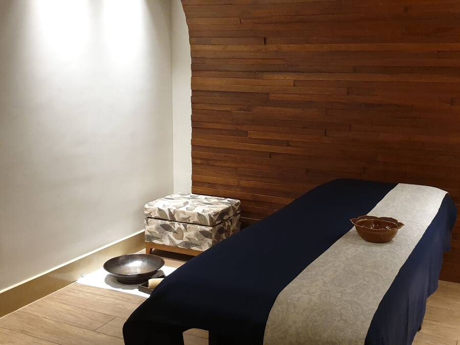 A room with a massage table, a small stool with a bowl, and a wooden wall.