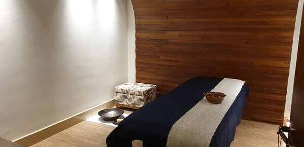 A room with a massage table, a small stool with a bowl, and a wooden wall. - Novotel Kochi Infopark (Kanayannur)