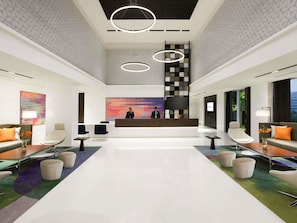 A modern hotel lobby with a reception desk, seating area, and a large abstract painting.