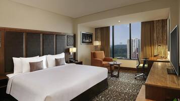 A hotel room with a large bed, a desk, a chair, a TV, and a window with a city view.