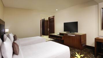 A hotel room with a bed, a TV, a desk, and a small table with a vase.