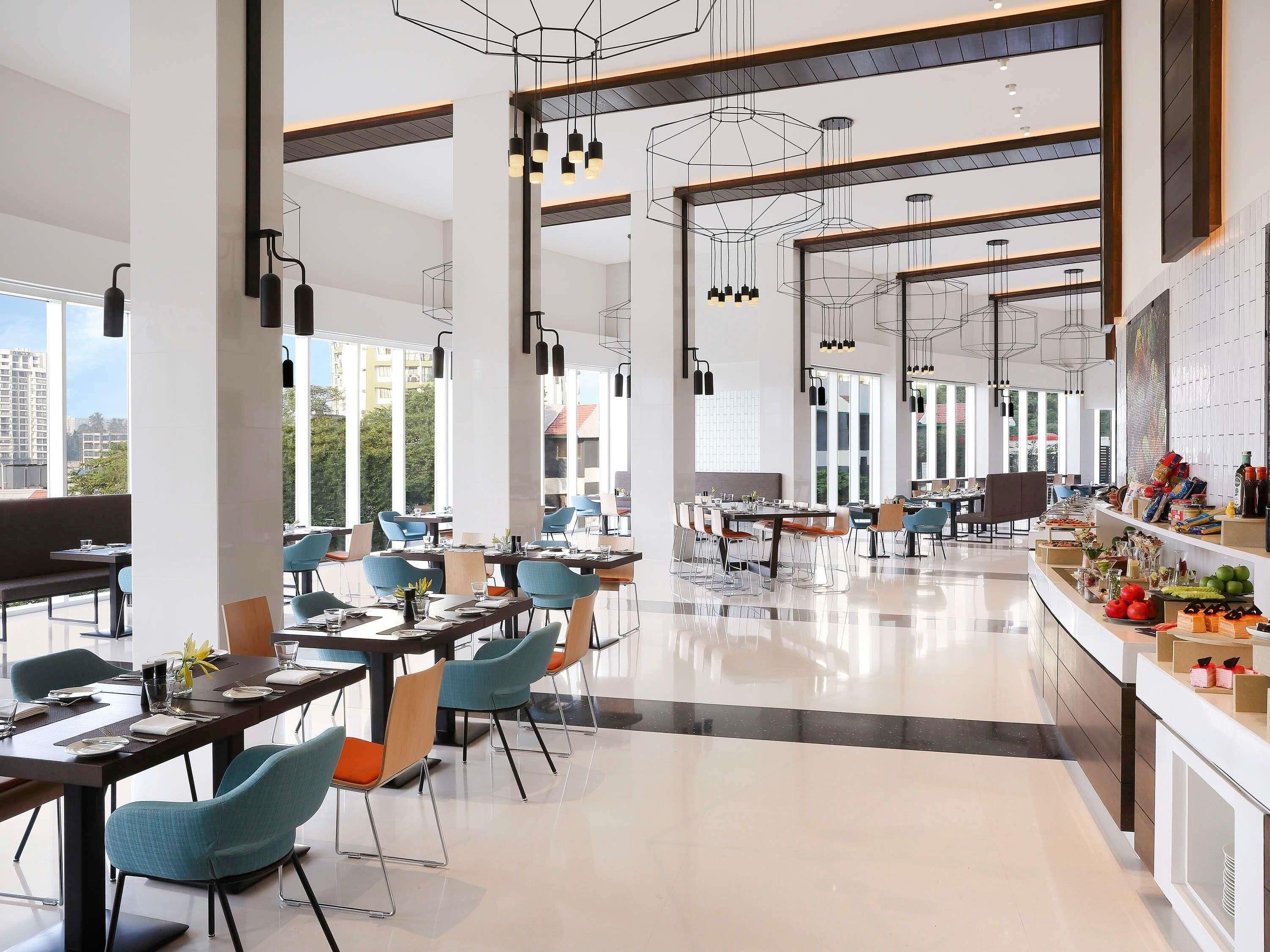 A modern dining area with high ceilings, pendant lighting, and a view of the cityscape.