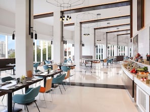 A modern dining area with high ceilings, pendant lighting, and a view of the cityscape.