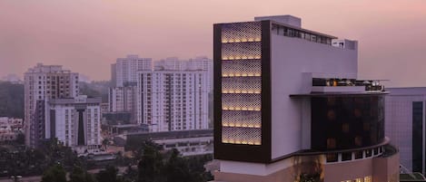 Een modern hotel met een opvallend verticaal lichtpaneel aan de gevel, een ruime binnentuin en uitzicht op omliggende hoogbouw.