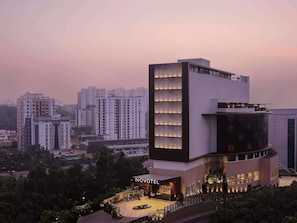 A modern hotel with a prominent vertical light panel on the facade, a spacious courtyard, and a view of surrounding high-rise buildings.
