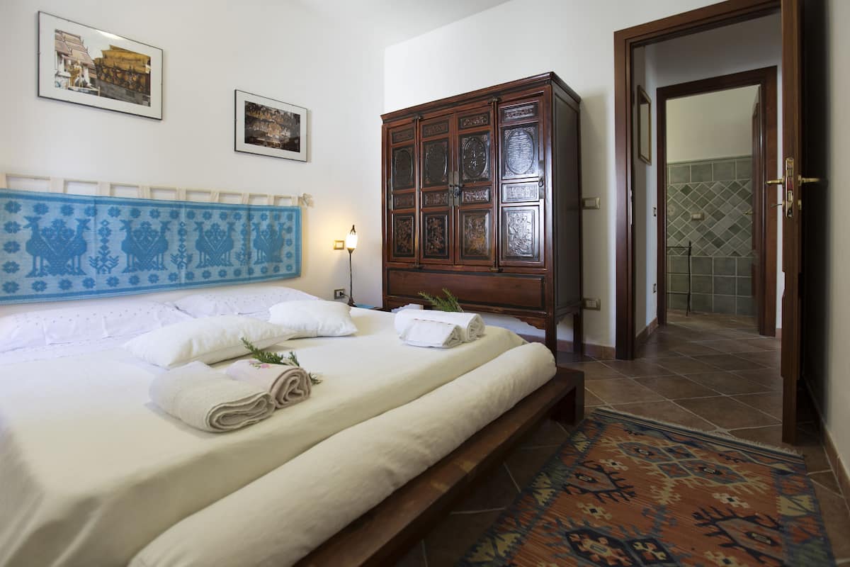 Una cama bien hecha con toallas, un armario de madera y un tapete estampado en una habitación de hotel.