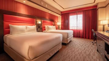 A hotel room with two beds, a desk, and a large window with red curtains.