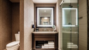 Un baño moderno con inodoro, lavamanos con espejo y cabina de ducha con mampara de vidrio.